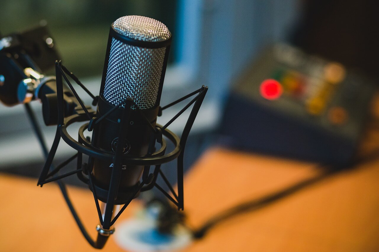 podcast e strikes - imagem de um microfone preto, em um braço articulado e no fundo uma imagem de um estúdio desfocado