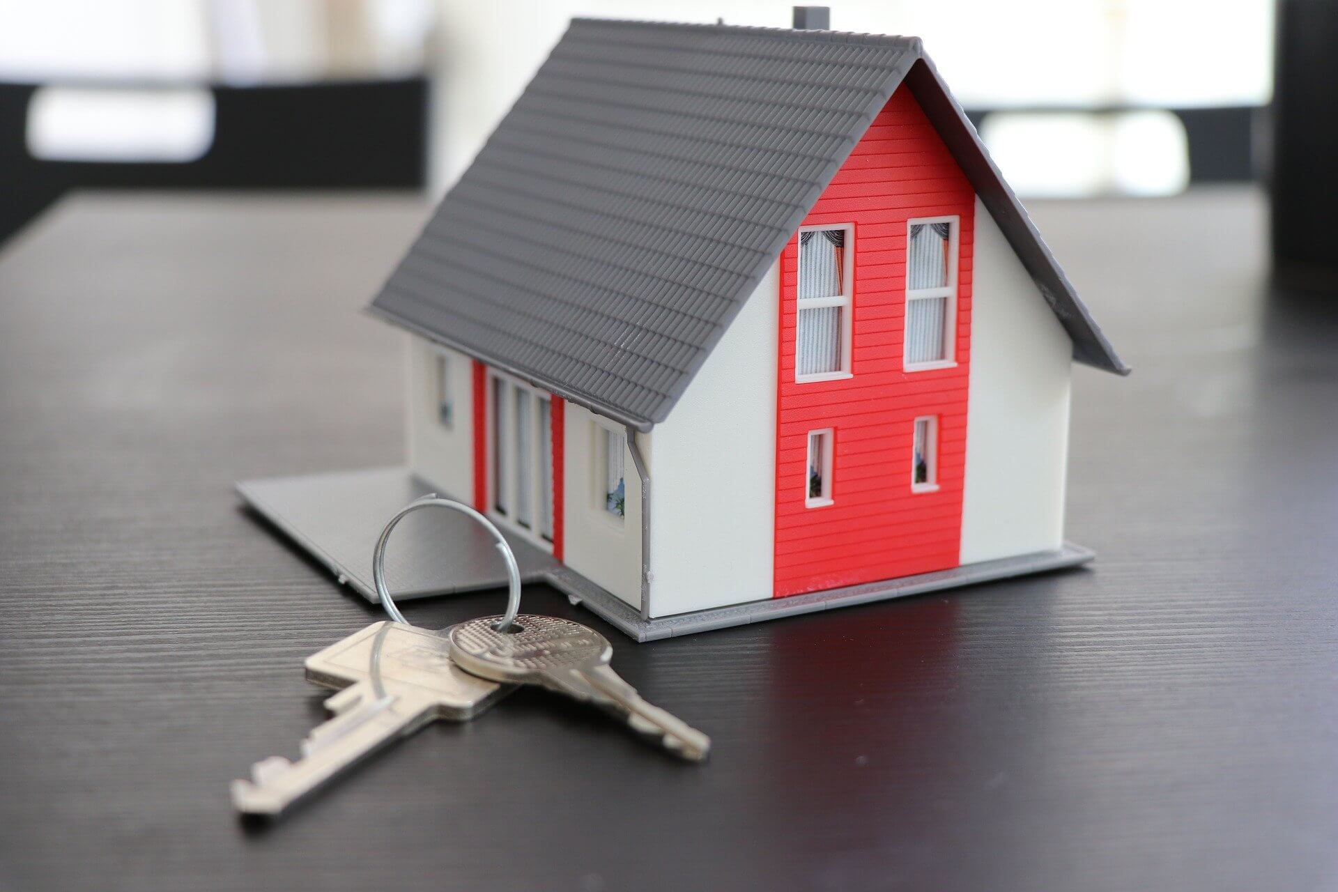 comprar casa 1 - uma maquete de uma casa cinza e vermelha sobre uma mesa de madeira escura e um molho de chaves