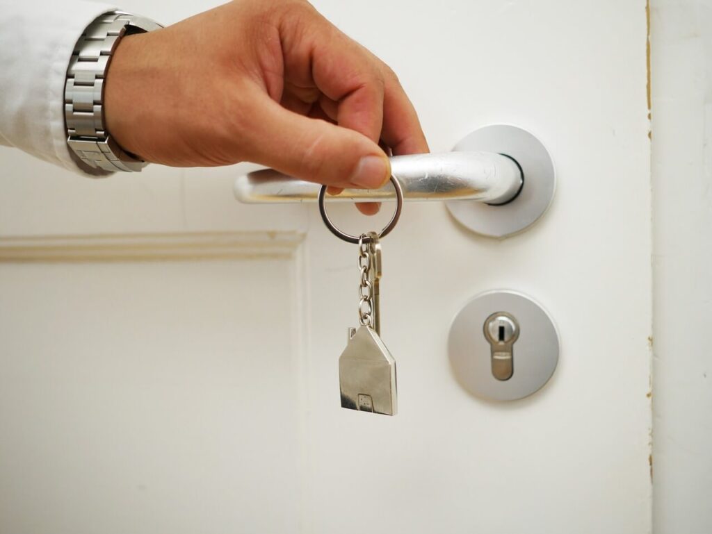 Airbnb 1 - imagem de uma porta branca com uma mão de um homem branco segurando uma chave prateada