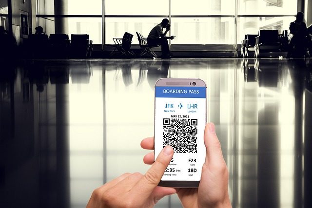 123 Milhas - imagem de um homem aguardando um voo no aeroporto, sentando em uma cadeira, mexendo em seu celular