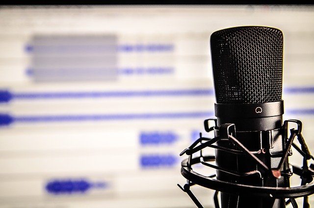 podcast e strikes 2 - foto de um microfone articulado de estúdio e, de fundo, uma tela de computador com um programa de edição de áudio aberto